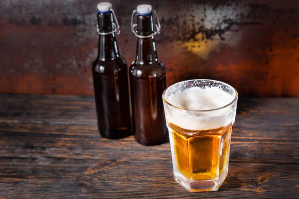 Two beer bottles near glass with a light beer and a head of foam