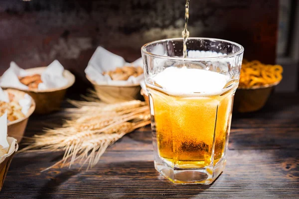 Beer is pouring into a glass near plates with pistachios, small — Stock Photo, Image