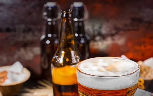 Cabeza de espuma de cerveza en vidrio cerca de botellas y platos con pistachi — Foto de Stock