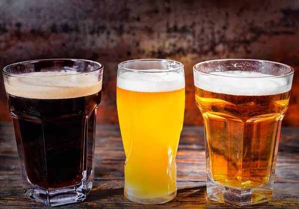 Три стакана с легким, нефильтрованным и темным пивом на темном лесу — стоковое фото