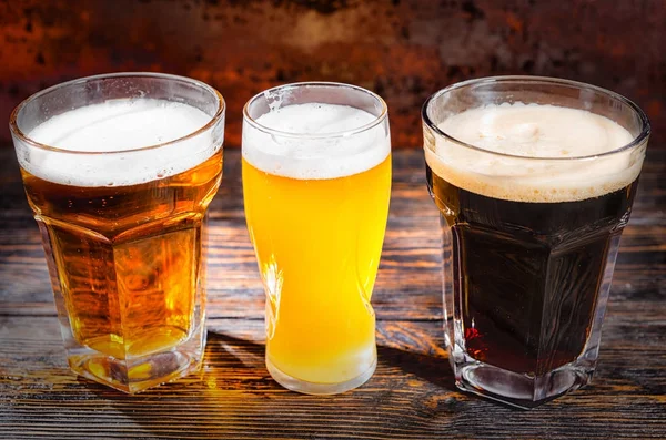 Three glasses with light, unfiltered and dark beer on wooden des — Stock Photo, Image