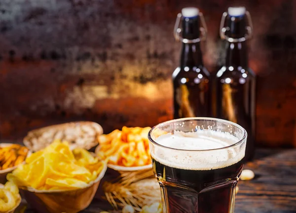 Platos con bocadillos cerca de dos botellas y un vaso de cerveza oscura, wh — Foto de Stock