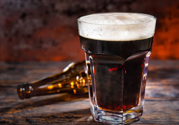 Pohár frissen öntött sötét sör közelében üres palackot a sötét fa — Stock Fotó