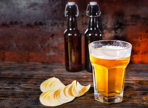Большой стакан светлого пива на фоне двух пивных бутылок рядом с чипсами на г — стоковое фото