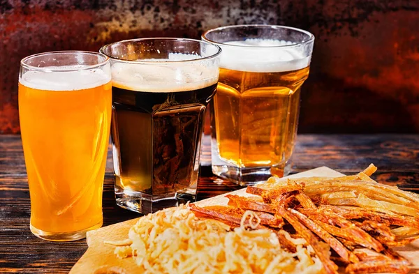 Three glasses with light, unfiltered and dark beer stand near wo — Stock Photo, Image