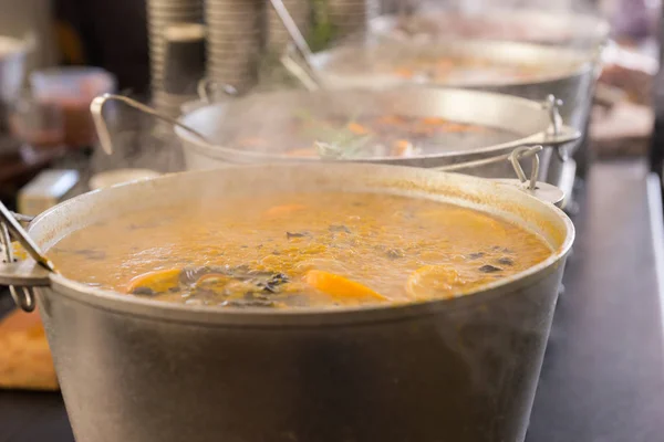 Пряный суп в больших котлах с ковшами внутри на открытой пище — стоковое фото