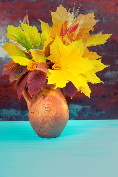 Prachtige clay kruik met herfstbladeren en tarwe op blauwe houten d — Stockfoto