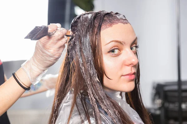 Mujer joven se sienta en una silla durante el proceso de teñir el cabello y lo — Foto de Stock