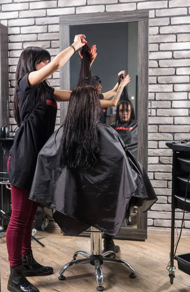 Female professional hair stylist with tattooed hands cutting and