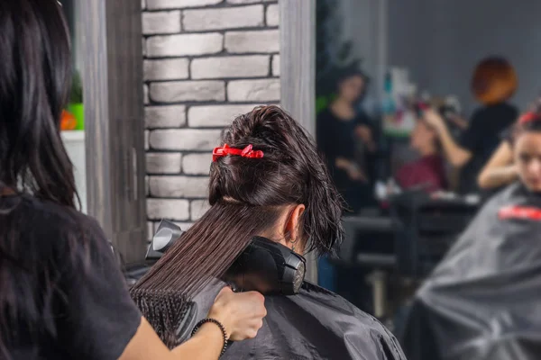 Beautiful hairdresser combing and using hair dryer on hair of yo — Stock Photo, Image