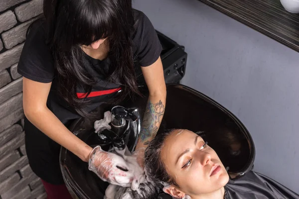 Mulher morena tendo o cabelo lavado e ensaboado pelo estilista feminino — Fotografia de Stock