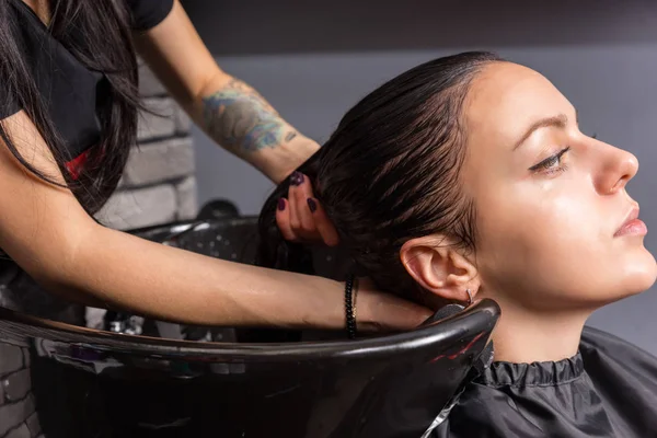 Молодая брюнетка, волосы которой стирает парикмахер — стоковое фото
