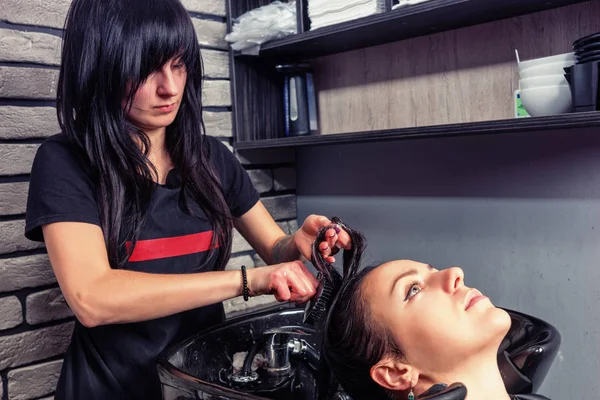 Peluquería morena peinando el pelo de la joven hermosa mujer en wa — Foto de Stock