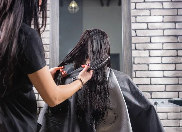 Estilista profesional femenina peinando el pelo mojado de joven morena w — Foto de Stock