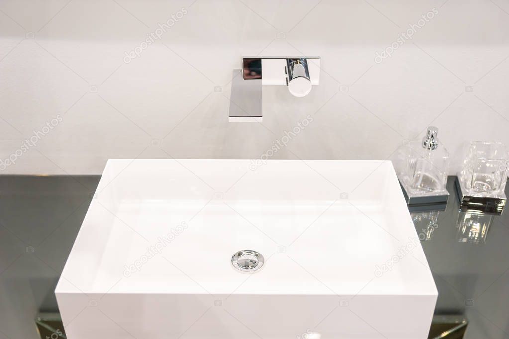 Modern square washbasin near glass containers for soap