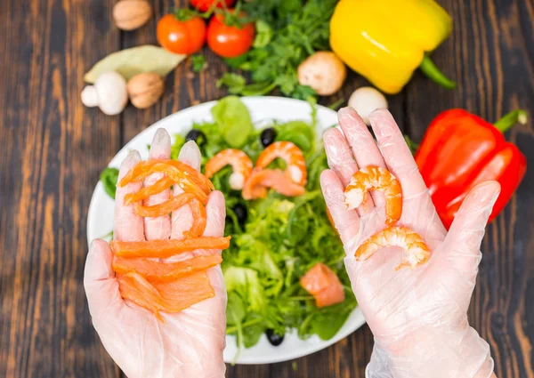 Close up of hands in gloves holding salmon in one hand and shrim — Stock Photo, Image