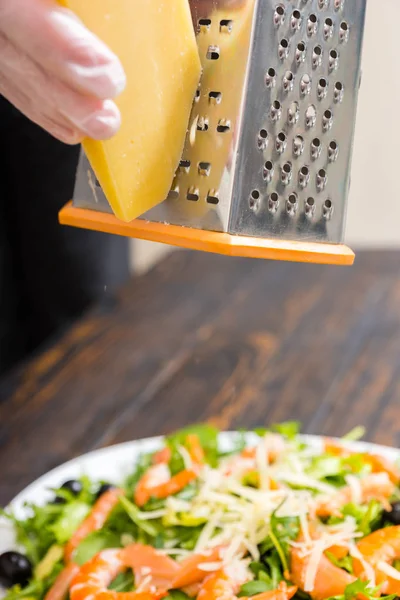 Hands in gloves rub cheese on a grater above salad with mix of l — Stock Photo, Image
