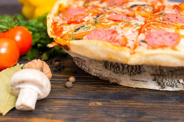 Pizza z salami, szynka, grzyby i warzywa na drewniany stojak — Zdjęcie stockowe
