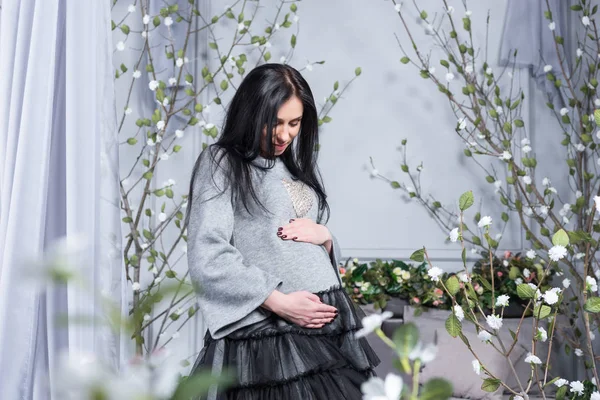 Mulher morena muito grávida mantendo as mãos na barriga de pé n — Fotografia de Stock