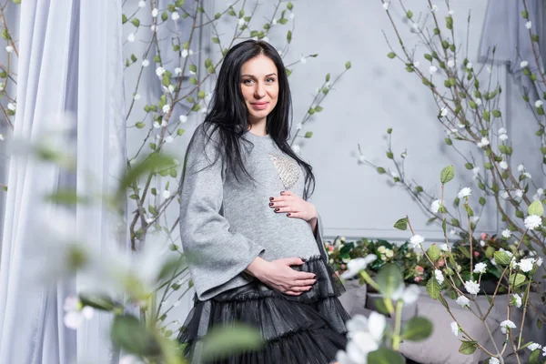 Adorável grávida morena mantendo as mãos na barriga de pé — Fotografia de Stock