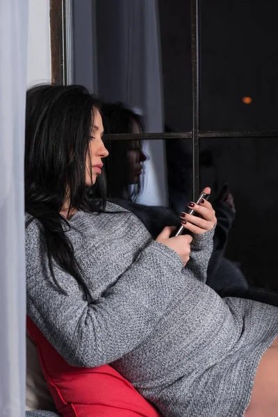 Attraktive schwangere brünette Frau in einem Strickkleid sitzt auf th — Stockfoto