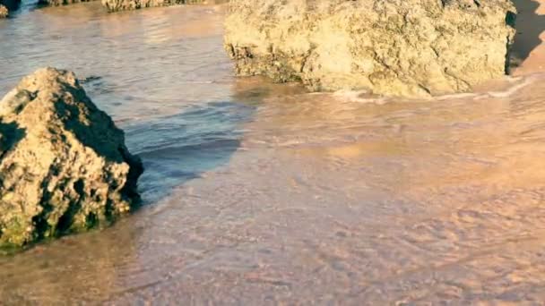 Surf golpeando las rocas en una playa de arena — Vídeos de Stock
