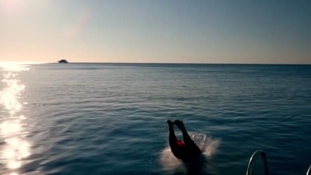 Homme plongeant dans la mer depuis un bateau au coucher du soleil — Video