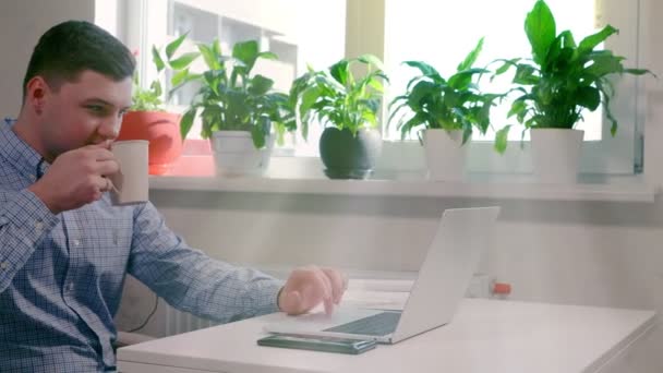Mladý muž pití kávy při práci na notebooku — Stock video