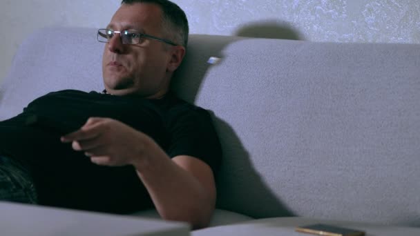 Man reclining on a couch watching television — Stok video