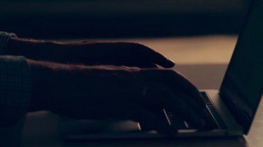 Hands of a man working on a laptop in darkness