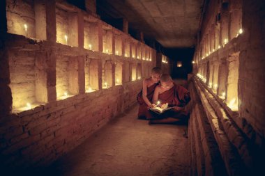 Genç Budist rahibeler, Mandalay tarihi parkında heykeli olan Bagan Mandalay, Myanmar 'ın dışında ve içinde mum ve güneş ışığı bulunan bir kitap okuyorlar.