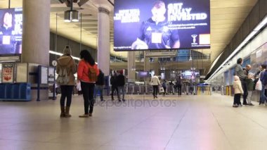 Londra, İngiltere, Birleşik Krallık - Nisan, 2017: Erkek, kadın ve Canary Wharf metro, tüp veya metro istasyonu bileti, yürüyüş, bekleyen veya acele aile; iki büyük ekran reklam videoları göster