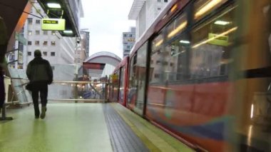 Arka görünümü platformunda, tren yürüyen adam ve genç bir çift Londra'da Heron Quays istasyondan kalkıyor     