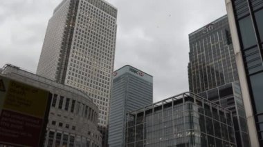 Londra, İngiltere, Birleşik Krallık - Nisan, 2017: El kamera eğimli atış şehir Canary Wharf Finans Merkezi bina ve Dlr istasyonu platformu insanlardan bulutlu gün
