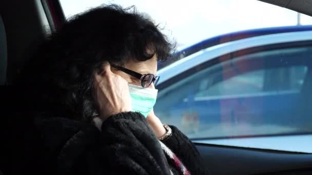 車の中に眼鏡をかけた熟女は ウイルスから保護し 駐車場に駐車車両から抜け出すためにフェイスマスクをつけています ビューを閉じる — ストック動画