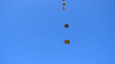 Düşük açılı pek çok bozuk para mavi gökyüzüne doğru yavaş çekimde düşüyor..