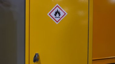 Bir adamın eli, içinde gaz tüpü olan sarı renkli metal kutu kutusunu açıyor. Yanıcı maddeleri ve alev sembolü etiketi olan malzemeleri saklamak için güvenli bir depo..