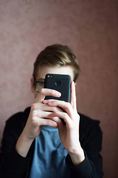 boy in glasses hide behind black smartphone and filming or gaming.