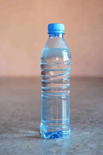 Blue plastic bottle of water on grey table on pink background.