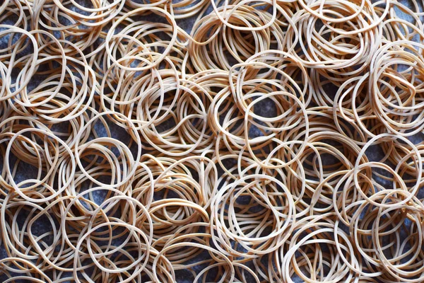 Stack of beige elastic rubber bands on grey table surface as abstract background.