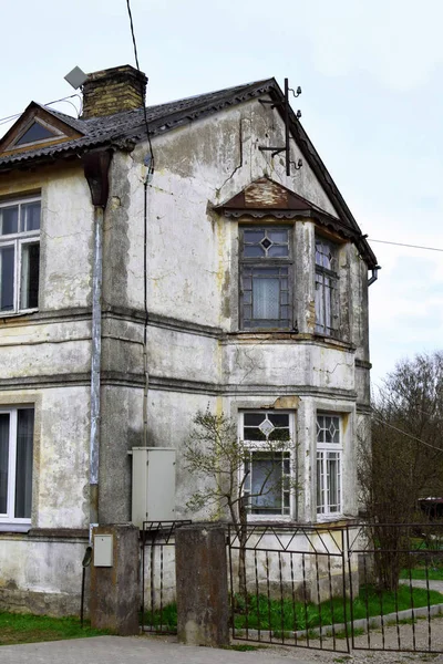 Old grey residential house with damaged plaster facade and old decorative wooden windows waiting for renovation.