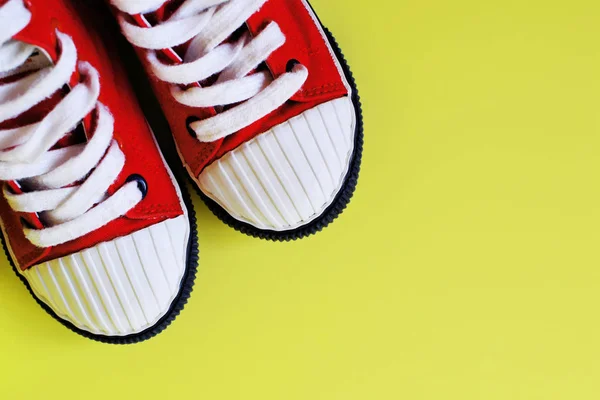 Pair of red kid canvas fabric sneakers on bright yellow background with copy space for text as template for greeting card.