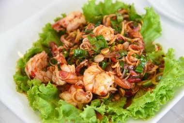 Baharatlı salata, domuz eti, kabuklu deniz ürünleri ve sebze bir restoranda masanın üstünde.