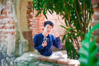 Elinde kamerayla bahçede mutlu bir şekilde gülümseyen mavili adam.