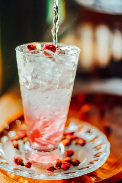 Iced Rose syrup with soda topped with rose petals on wood table, Summer refreshment drinks