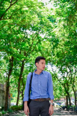 Mutlu Asya 'lı adam yeşil çalıların arka planında duran bir portre için kameraya bakıyor.