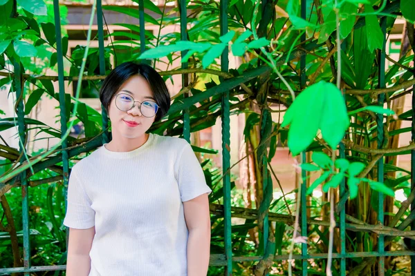 Happy Asia woman wearing glasses is looking into the camera for a portrait on the street on a background of green bushes