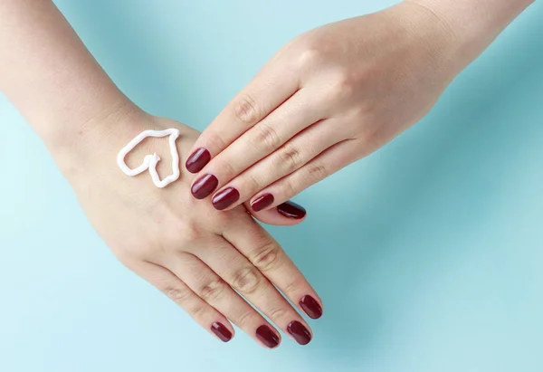 Creme na forma de um coração na mão feminina com manicure vermelho, fundo azul pastel, vista superior — Fotografia de Stock