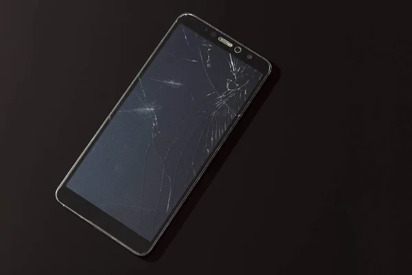 Broken smartphone screen with cracks close-up on a black background — Stock Photo, Image