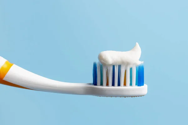 Escova de dentes com pasta de dentes branca close-up no fundo azul — Fotografia de Stock
